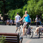 Фото тату на плече и руке мужчины, едущего на велосипеде. Вид сзади, солнечный день, городская сцена.