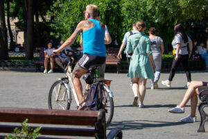 Фото тату на плече и руке мужчины, едущего на велосипеде по парку. Вид сзади, солнечный день, городская сцена.
