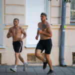два парня с голым торсом и татуировками на теле бегают в центре города.m