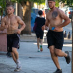 Фотография мужчины, бегущего по улице с обнаженным торсом, на котором видны небольшие татуировки. Он одет в спортивные шорты и наушники.