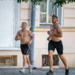 Фотография мужчины, бегущего по улице с обнаженным торсом, на котором видны небольшие татуировки. Он одет в спортивные шорты и наушники.