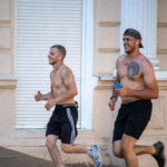 два парня с голым торсом и татуировками на теле бегают в центре города5050