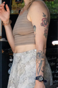 Крупный план руки девушки, украшенной татуировками в виде роз с лицами, морского якоря и других элементов. Яркий и детализированный рисунок.