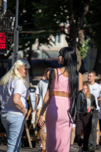 Фото тату: реалистичная татуировка розы с листьями на плече девушки в розовом костюме на улице.
