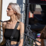 Фотография молодой женщины с татуировкой на руке, смотрящей в сторону. Современный городской стиль.