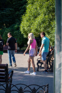 Фото тату: Девушка с яркой японской татуировкой на руке, изображающей гейшу и цветы, идущая по улице в окружении людей.