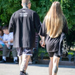Фотография пары, идущей по улице, демонстрирующая татуировки на руках и ногах мужчины и татуировку на лодыжке женщины. Солнечный день.