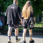 Фотография мужчины и женщины, идущих по улице, держась за руки. У мужчины видны татуировки на руках и шее, у женщины - на ноге.