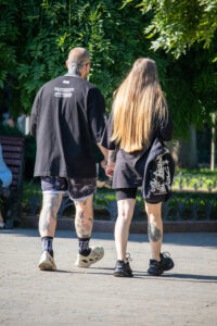 Фотография мужчины и женщины, идущих по улице, держась за руки. У мужчины видны татуировки на руках и шее, у женщины - на ноге.