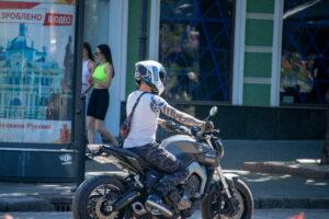 Фото мотоциклиста в шлеме с татуировкой на руке, едущего по улице.