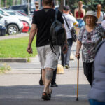 Фото мужчины с татуировкой на икре, идущего рядом с пожилой женщиной с тростью.