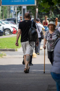 Фото мужчины с татуировкой на икре, идущего рядом с пожилой женщиной с тростью.