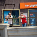 Фото двух мужчин с татуировками на руках, стоящих на балконе. Видны татуировки на руках, белые и красные футболки.