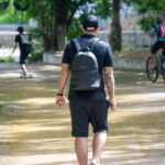 Фото тату на руке мужчины, идущего по парковой аллее. Вид сзади, татуировка в стиле традишнл.