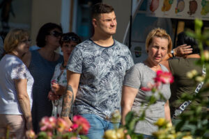 Фото тату на руке мужчины, изображающее лицо монахини в черном головном уборе, на фоне людей и киоска с мороженым.