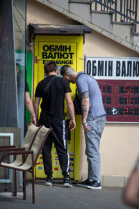Фотография мужчины с татуировкой на руке, стоящего у обменного пункта. Татуировка выполнена в темных тонах и имеет сложный узор.