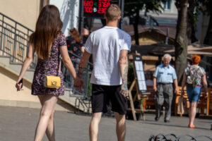 Фото пары, идущей по улице. У мужчины видны татуировки на руке, акцент на татуировках и летней атмосфере.