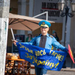 пожилой мужчина в одежде Супергероя стилизованное под флаг Украины и надписью сделай что-нибудь полезное для Украины35