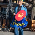 пожилой мужчина в одежде Супергероя стилизованное под флаг Украины и надписью сделай что-нибудь полезное для Украины5354