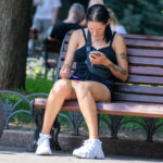 Фотография девушки, сидящей на скамейке и смотрящей в телефон. На плече и руке видны татуировки с растительным мотивом.
