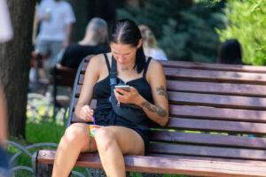 Фотография девушки, сидящей на скамейке и смотрящей в телефон. На плече и руке видны татуировки с растительным мотивом.