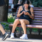 Фотография девушки, сидящей на скамейке и смотрящей в телефон. На плече и руке видны татуировки с растительным мотивом.