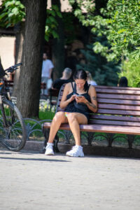 Фотография девушки, сидящей на скамейке и смотрящей в телефон. На плече и руке видны татуировки с растительным мотивом.