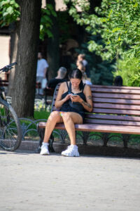 Фотография девушки, сидящей на скамейке и смотрящей в телефон. На плече и руке видны татуировки с растительным мотивом.