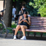 Фотография девушки, сидящей на скамейке и смотрящей в телефон. На плече и руке видны татуировки с растительным мотивом.