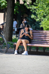 Фотография девушки, сидящей на скамейке и смотрящей в телефон. На плече и руке видны татуировки с растительным мотивом.
