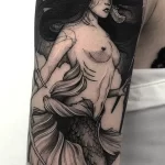 Фото татуировки на руке с изображением русалки с рогами, выполненной в стиле blackwork с использованием плотных черных линий.