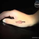 Фотография небольшой цветной татуировки на стопе, изображающей зажигалку с вырывающимся пламенем. Татуировка выполнена в ярких красных и оранжевых тонах.