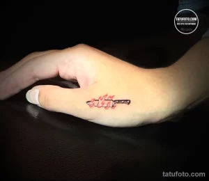 Фотография небольшой цветной татуировки на стопе, изображающей зажигалку с вырывающимся пламенем. Татуировка выполнена в ярких красных и оранжевых тонах.