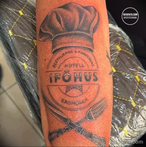 Фото тату на предплечье с изображением винтажной вывески ресторана 'IFOHUS', выполненное в стиле старой школы.