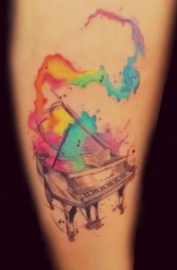 Фото тату: Акварельный рисунок пианино с яркими радужными брызгами на предплечье. Идеально для любителей музыки и искусства.