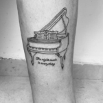 Фото тату: Простая черно-белая татуировка пианино с надписью "The right music is everything" на ноге. Минималистичный и вдохновляющий дизайн.