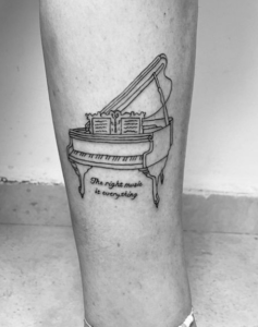 Фото тату: Простая черно-белая татуировка пианино с надписью "The right music is everything" на ноге. Минималистичный и вдохновляющий дизайн.