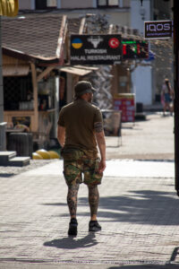 Фото мужчины с татуировками на ногах и руке на фоне города: масштабные татуировки в стиле ориентал с изображением черепа, карпа кои и геометрических узоров. Стильный образ.