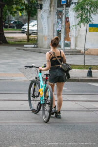 Фото тату на плече девушки, стоящей с велосипедом на городской улице. Рисунок татуировки выполнен в черных тонах, изображает абстрактный узор.