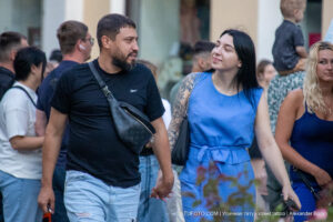 Фото пары: мужчина в черной футболке и джинсовых шортах, женщина в голубом платье с татуировкой на руке. Уличная фотография, демонстрирующая татуировки в повседневной жизни.