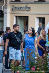 Фото пары: мужчина в черной футболке и джинсовых шортах, женщина в голубом платье с татуировкой на руке. Уличная фотография, демонстрирующая татуировки в повседневной жизни.