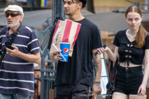 Фотография мужчины с татуировками на руках, держащего стакан и пакет с едой. Видны тату в стиле графика и небольшое тату сердца.