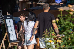 Фотография пары, идущей по улице. У мужчины и женщины видны татуировки на руках, выполненные в разных стилях. Летний день.