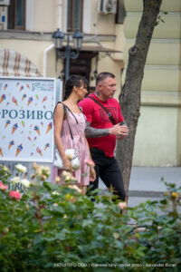 Фотография мужчины с татуировкой на руке, идущего рядом с женщиной на улице. Татуировка выполнена в черном цвете и покрывает большую часть руки.