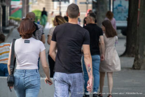 Фотография мужчины и женщины, идущих по улице. У мужчины на руке видна татуировка с изображением розы и надписи.