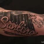 Фото тату на руке с изображением клавиш пианино и надписью "Santino". Детализированный рисунок татуировки в черно-серых тонах.