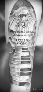 Фото татуировки на руке с изображением лестницы, ведущей в свет, с религиозным символом и надписью на латыни. Черно-белый рисунок с детальной проработкой теней.