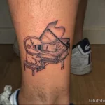 Небольшое черно-белое тату на ноге с изображением космонавта, играющего на пианино. Стиль - минимализм, контурная графика.