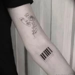 Фото татуировки в стиле one line с изображением пианино и роз на руке. Черно-белый рисунок татуировки.
