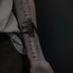 Фото тату на руке: рояль и нотная запись, выполненные в технике blackwork. Детализированный рисунок с использованием тонких линий.